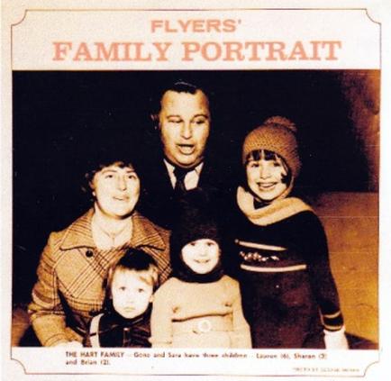 A family portrait of a family. It is a black and white photograph of a man a woman and three children. The man is in the center of the image with the woman on the left and the children on the right. The woman is wearing a plaid coat and a hat while the children are wearing winter clothes and hats. The children are smiling and looking at the camera. The background is blurred but it appears to be a room with a window. The text on the image reads "Flyers' Family Portrait" and "The Hart Family - Gone and Gone Gone and Gone with the Children Lauren Sharon and Brian."