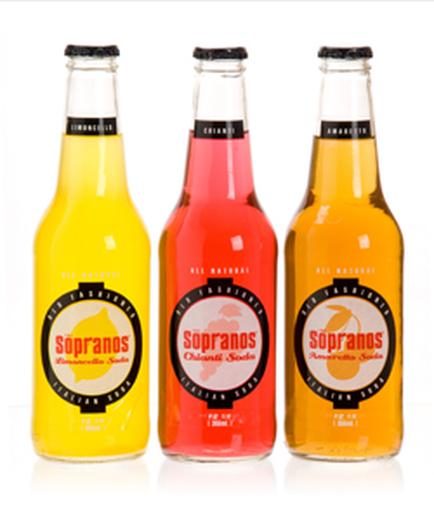 Three bottles of Sopranos sparkling water. The bottles are arranged in a row with the first bottle on the left being yellow the middle bottle being pink and the third bottle being orange. All three bottles have a black label with the word "sopranos" written in white capital letters. The label also has a small illustration of a grapefruit in the center. The background is white.