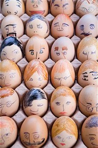 A tray of eggs with multiple faces drawn on them. The eggs are arranged in a grid-like pattern and are of different sizes and shapes. Each egg has a unique expression on its face ranging from happy to sad surprised to angry. Some of the faces have different facial expressions including eyes noses and mouths while others have more serious expressions. The colors of the eggs vary with some being light brown some being orange and some being black. The tray appears to be made of cardboard or cardboard and is placed on a white surface.