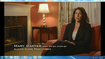 A screenshot from a video interview with Mary Carter MSN RN-BC apron-BC. She is sitting on a red armchair in a living room with a fireplace and a lamp in the background. Mary Carter is wearing a black blazer and a white blouse and she is looking directly at the camera with a serious expression on her face. The text on the image reads "Mary Carter M.N.RN-BC - apron - BC - Alicia's Nurse Practitioner".