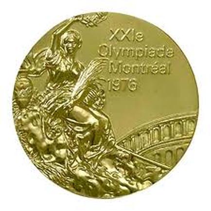 A round gold-colored medal with the text "XXIe olympiads montreal 1976" inscribed on it. The medal appears to be made of metal and has a smooth polished surface. On the left side of the medal there is an image of a statue of a woman holding a spear and shield with a castle in the background. The woman is wearing a long flowing dress and has her hair flowing in the wind. She is sitting on a throne-like structure with her legs crossed and her arms raised in the air. The statue is surrounded by a laurel wreath. The text is written in a cursive font and is in a dark color. The overall design is intricate and detailed.