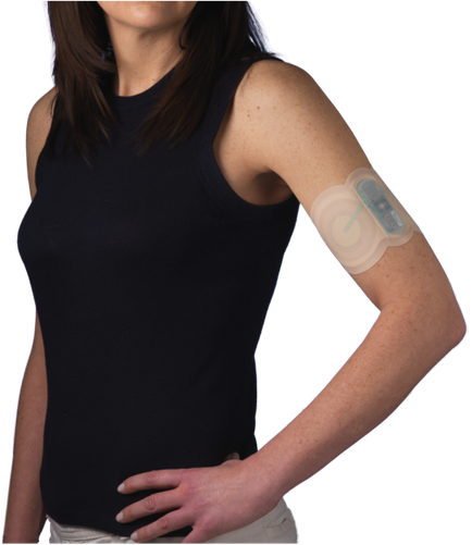 A young woman with shoulder-length brown hair wearing a black tank top. She is standing with her left arm slightly bent at the elbow and her right hand resting on her hip. On her arm there is a beige-colored bandage with a small electronic device attached to it. The device appears to be a medical device possibly a blood pressure monitor. The woman is looking away from the camera with a neutral expression on her face.