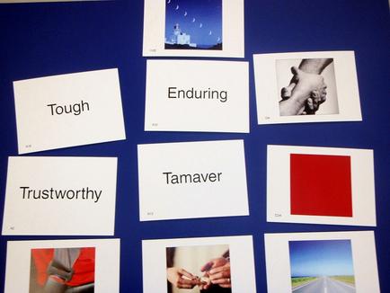 A collage of nine square photographs arranged in a grid-like pattern on a blue background. Each photograph is accompanied by a white card with the word "Tough" written on it in black text. The first photograph on the top left shows a lighthouse with a blue sky and white clouds in the background. The second photograph in the top right shows two hands holding each other with the words "Enduring" and "tamper" written above them. The third photograph is a black and white photograph of a person's hand holding a red square. The fourth photograph is of a road with a red rectangle in the center. The fifth photograph is from the bottom left corner of the collage showing a person wearing a red shirt and holding a pair of scissors. The sixth photograph is in the bottom right corner with a photograph of two hands reaching out towards each other. Overall the image conveys a sense of strength and resilience in the face of adversity.