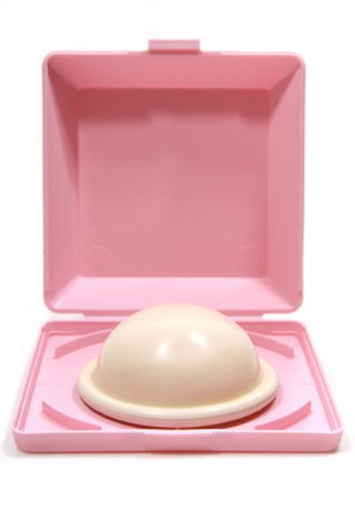 A pink plastic box with a lid. The lid is open revealing the interior of the box. Inside the box there is a white dome-shaped object which appears to be a toilet seat. The object is placed on a pink tray which is also pink in color. The tray has a handle on the top for easy carrying. The background is white.