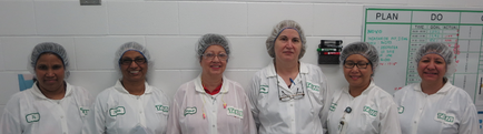A group of six women standing in a line in front of a whiteboard. They are all wearing white lab coats with green labels on them and hairnets on their heads. The women are smiling and appear to be in a laboratory or laboratory setting. On the right side of the image there is a green board with the words "PLAN" and "DO" written on it. The board appears to be a plan or plan of some kind.