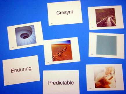 A collection of six polaroid photographs arranged in a grid-like pattern on a blue background. The photographs are arranged in two rows and three columns. The first photograph on the top left is a black and white photograph of a spiral staircase. The second photograph is a close-up of the staircase with the word "present" written above it. The third photograph is an aerial view of a train track with trees and buildings in the background. Next to the first photograph there is a white card with the words "Enduring" written in black text. The fourth photograph is of a group of people walking on a dirt road with a blue sky and clouds above them. The fifth photograph is from the top right corner of the image with an image of a person holding a dog. The sixth photograph is in the bottom right corner with another photograph in the center. The text below the photographs reads "Predictable".