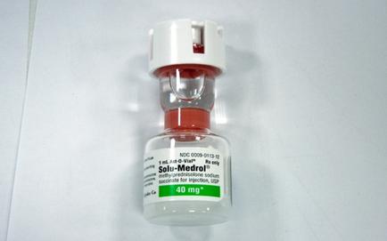 A small glass vial with a white cap. The vial is filled with a red liquid and has a label on it that reads "sold-Medrol" and "40 mg". The label also mentions that the vial contains 40 mg of sold-medrol. The cap is white and appears to be made of plastic. The background is plain white.